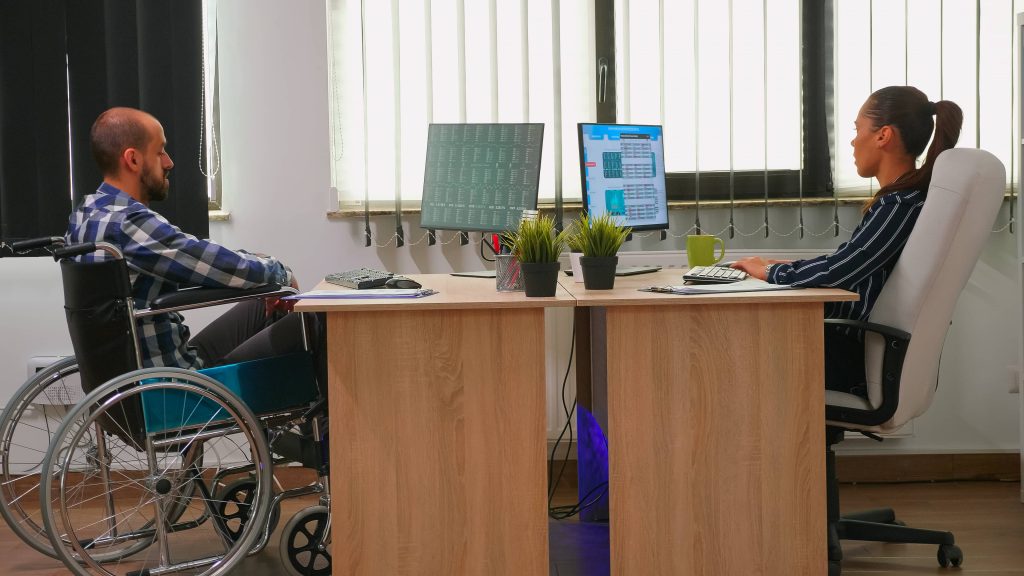 businesswoman-analysing-financial-statistics-talking-with-handicapped-coworker-sitting-wheelchair-checking-graphs-desk-building-office-disabled-businessman-using-modern-technology
